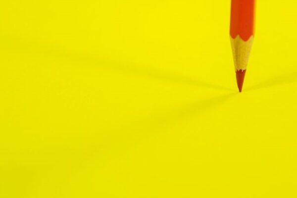 Tools zur Rechtschreibprüfung: Gelber Untergrund, darauf ein roter Buntstift, der mit der Spitze den gelben Untergrund berührt