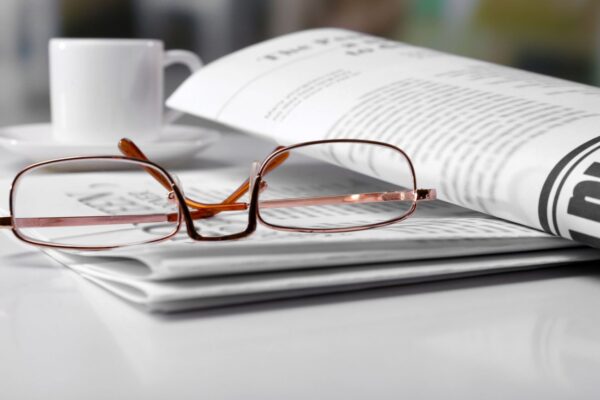 Werbetexte schreiben: weißer Schreibtisch mit mehreren Papieren, darauf eine Brille, dahinter eine weiße Kaffeetasse