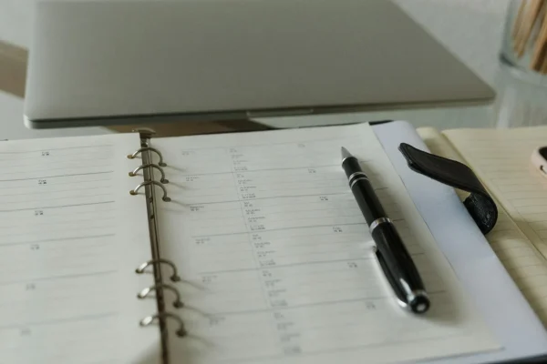 Datum richtig schreiben: Schreibtisch mit Notebook, davor ein geöffneter Kalender, in dem ein Kugelschreiber liegt