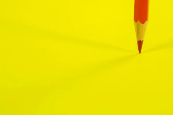 KI-Tools zur Rechtschreibprüfung: Gelber Untergrund, darauf ein roter Buntstift, der mit der Spitze den gelben Untergrund berührt