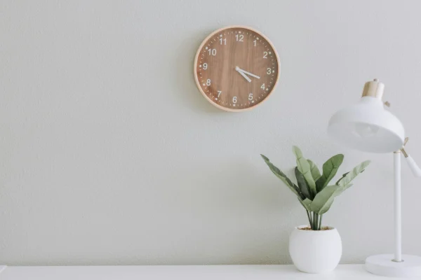 Uhrzeiten richtig schreiben: Schreibtisch mit Zimmerpflanze und Tischlampe, an der Wand im Hintergrund eine Wanduhr, die 16:19 Uhr anzeigt