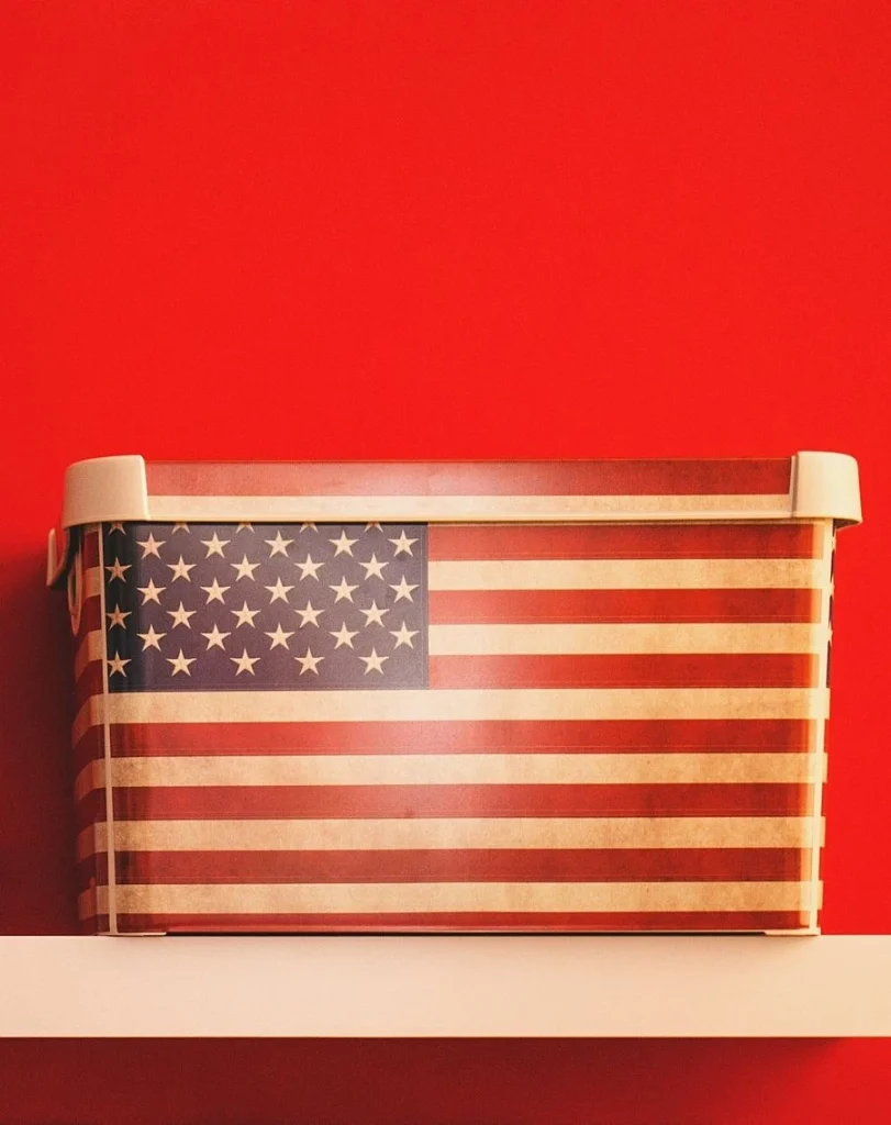 Rote Wand mit hellem Regalbrett: Darauf steht eine Box im Design der US-Flagge.